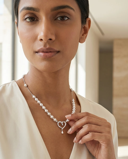 Woman wearing a delicate silver pearl necklace with a central heart pendant and matching earrings