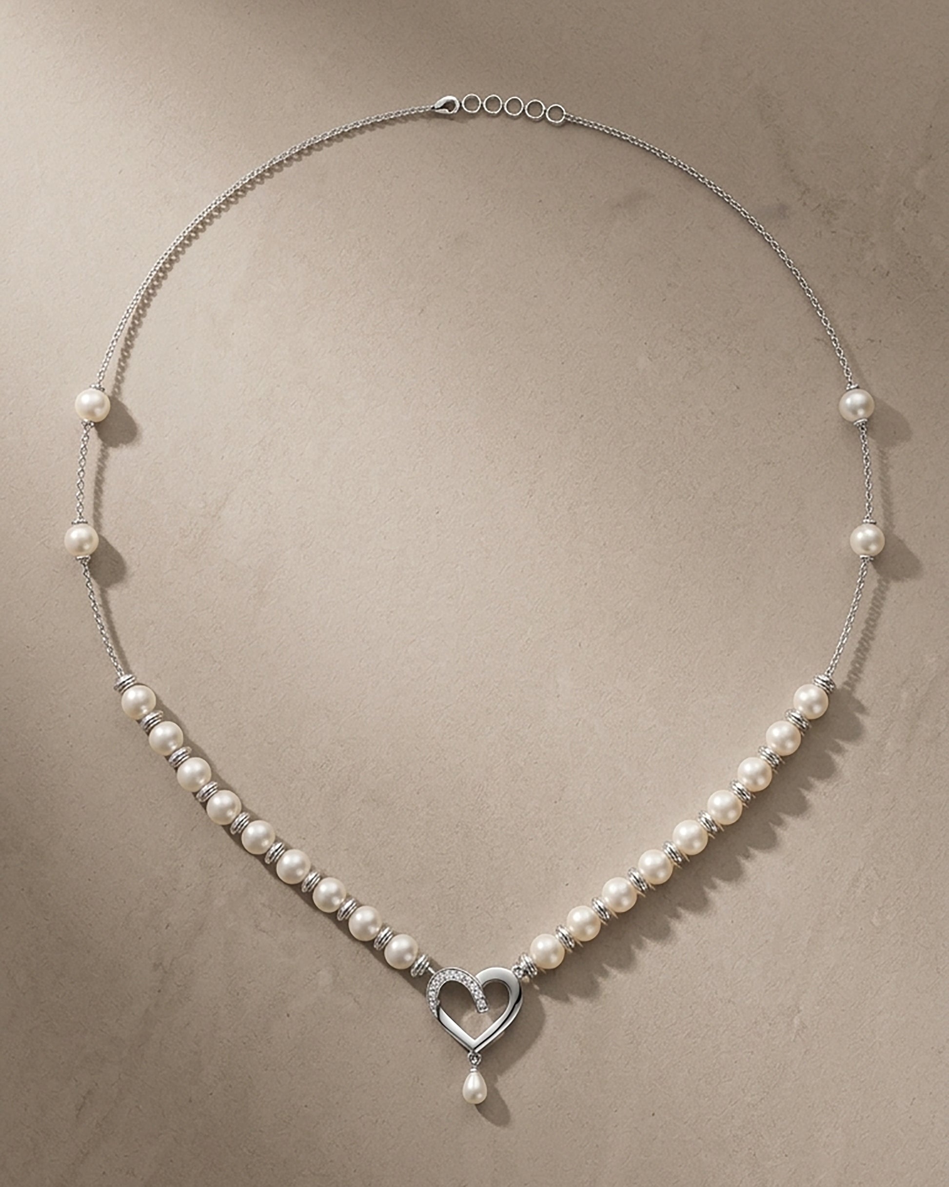 Minimalist overhead view of a silver necklace featuring white pearls and a heart-shaped centerpiece