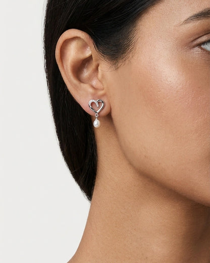 Close-up side profile of a woman wearing a silver heart-shaped stud earring with a pearl drop detail